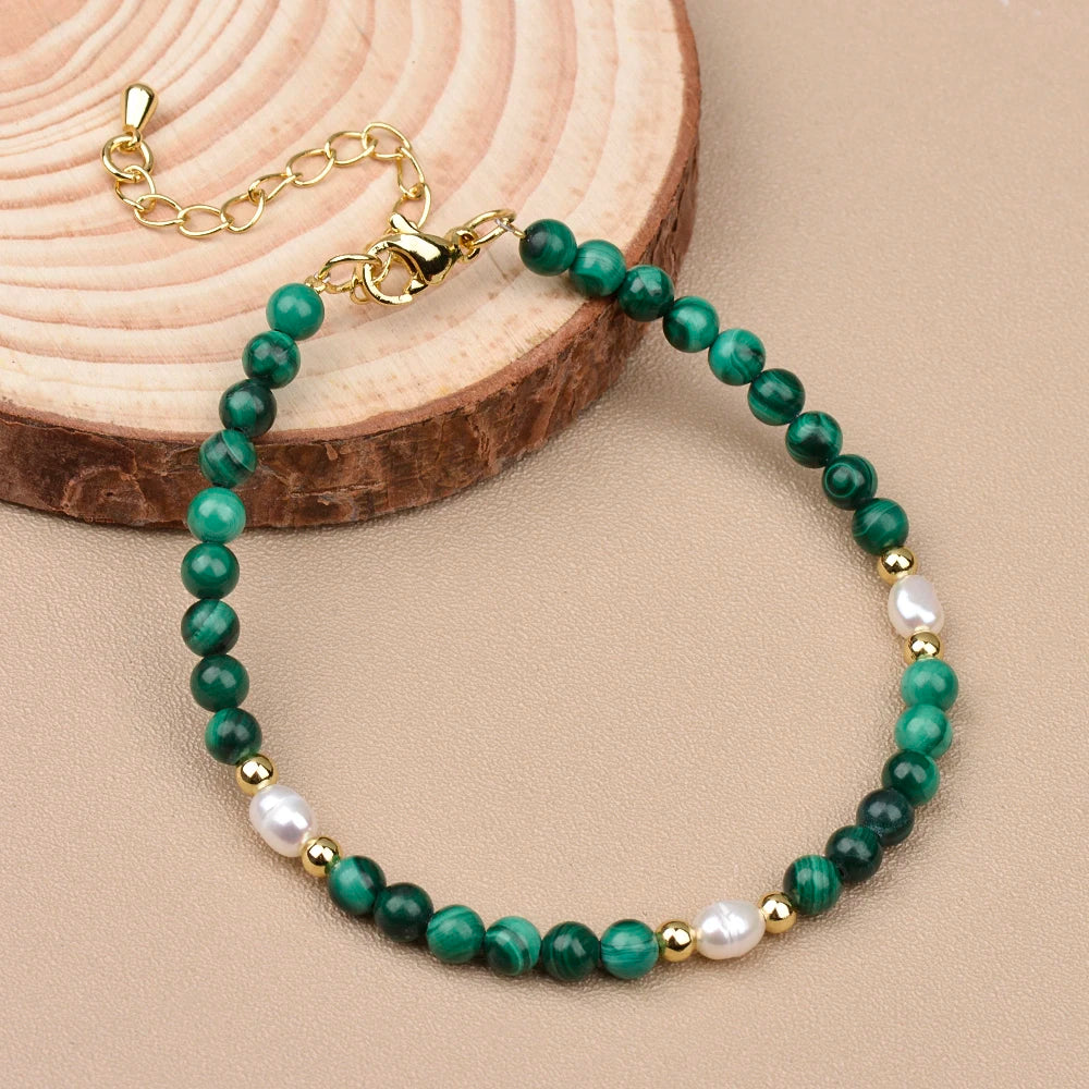 Malachite and pearl bracelet featuring green beads, gold accents, and a delicate design on a wooden surface.