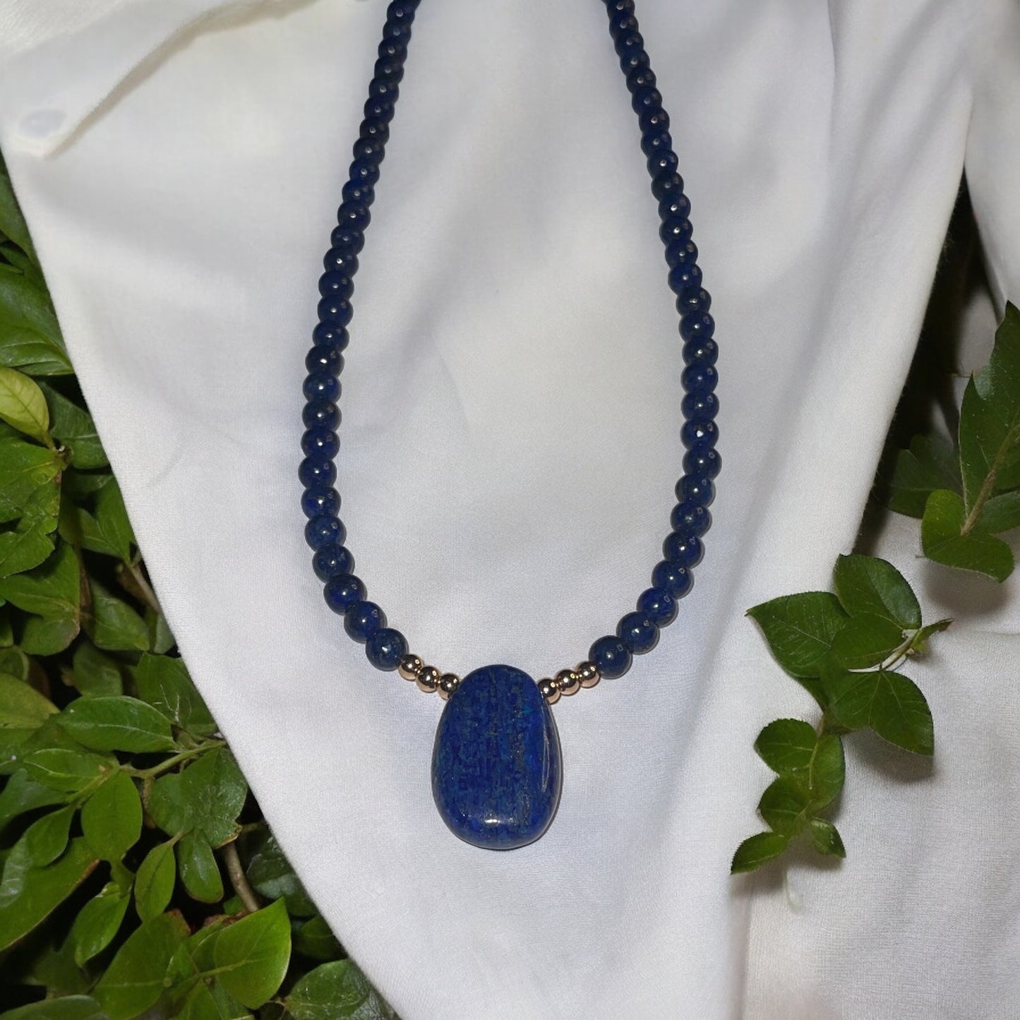 Handcrafted lapis lazuli pendant necklace featuring smooth beads and a polished centerpiece on a white fabric background.