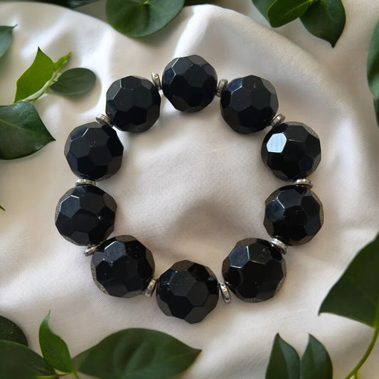 Chunky Obsidian bracelet with large faceted beads, surrounded by green leaves, on a soft white fabric.'Spiritual Armor' Chunky Obsidian Bracelet