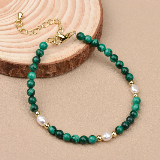 Malachite and pearl bracelet featuring green beads, gold accents, and a delicate design on a wooden surface.