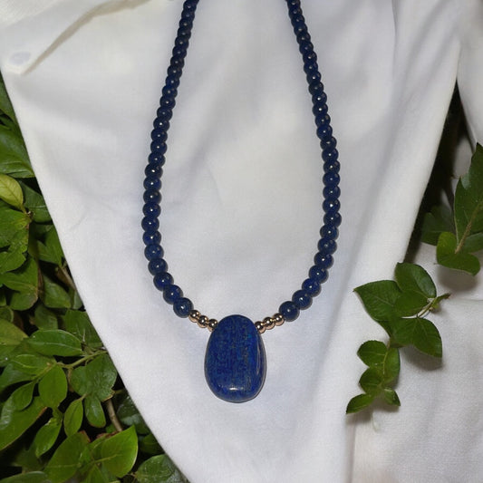 Handcrafted lapis lazuli pendant necklace featuring smooth beads and a polished centerpiece on a white fabric background.
