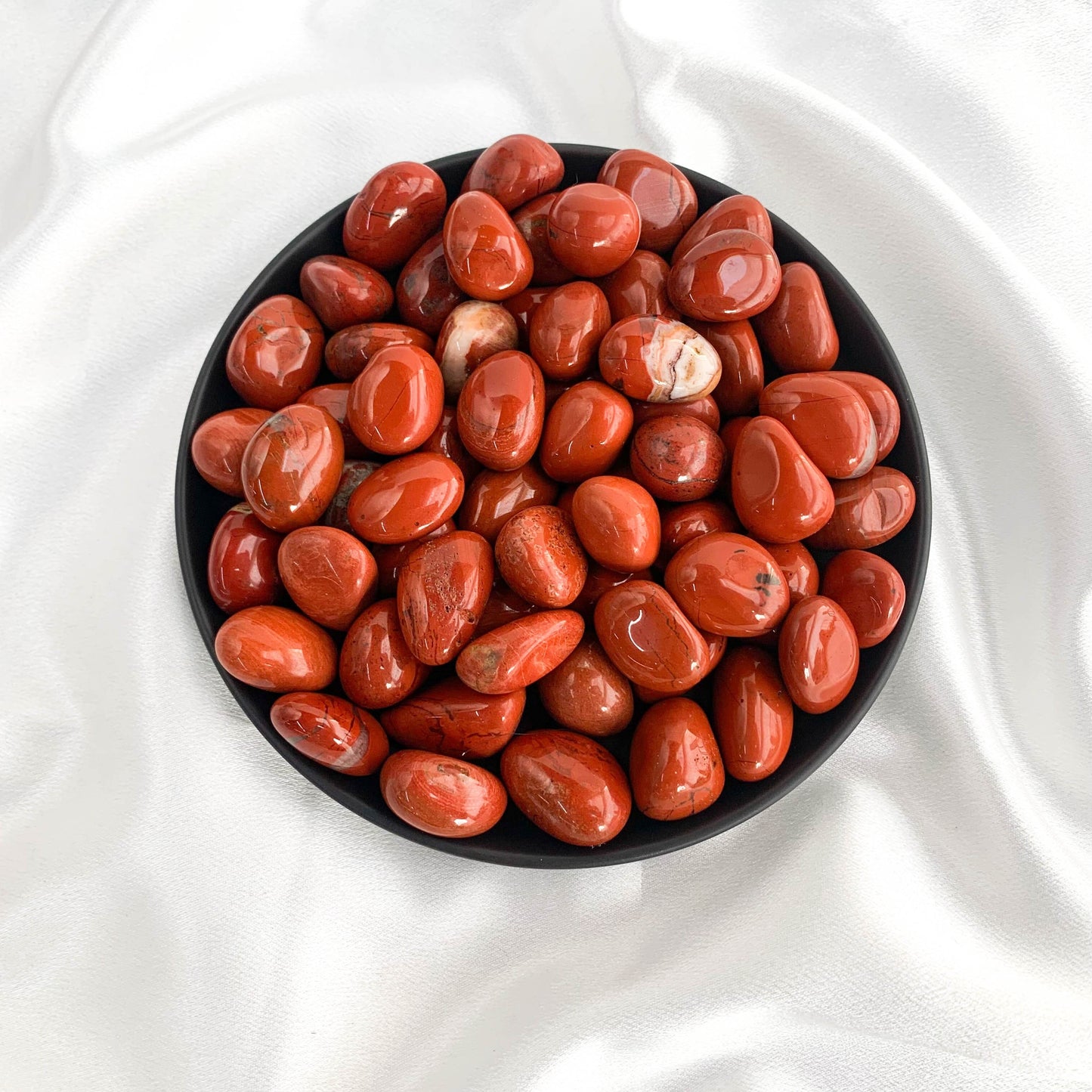 Bowl of polished red agate stones, showcasing their vibrant colors and smooth surface, ideal for grounding and strength.