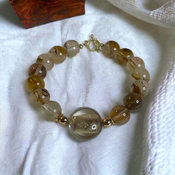 Golden Thread Rutilated Quartz bracelet with translucent beads and golden rutile inclusions on a soft fabric background.
